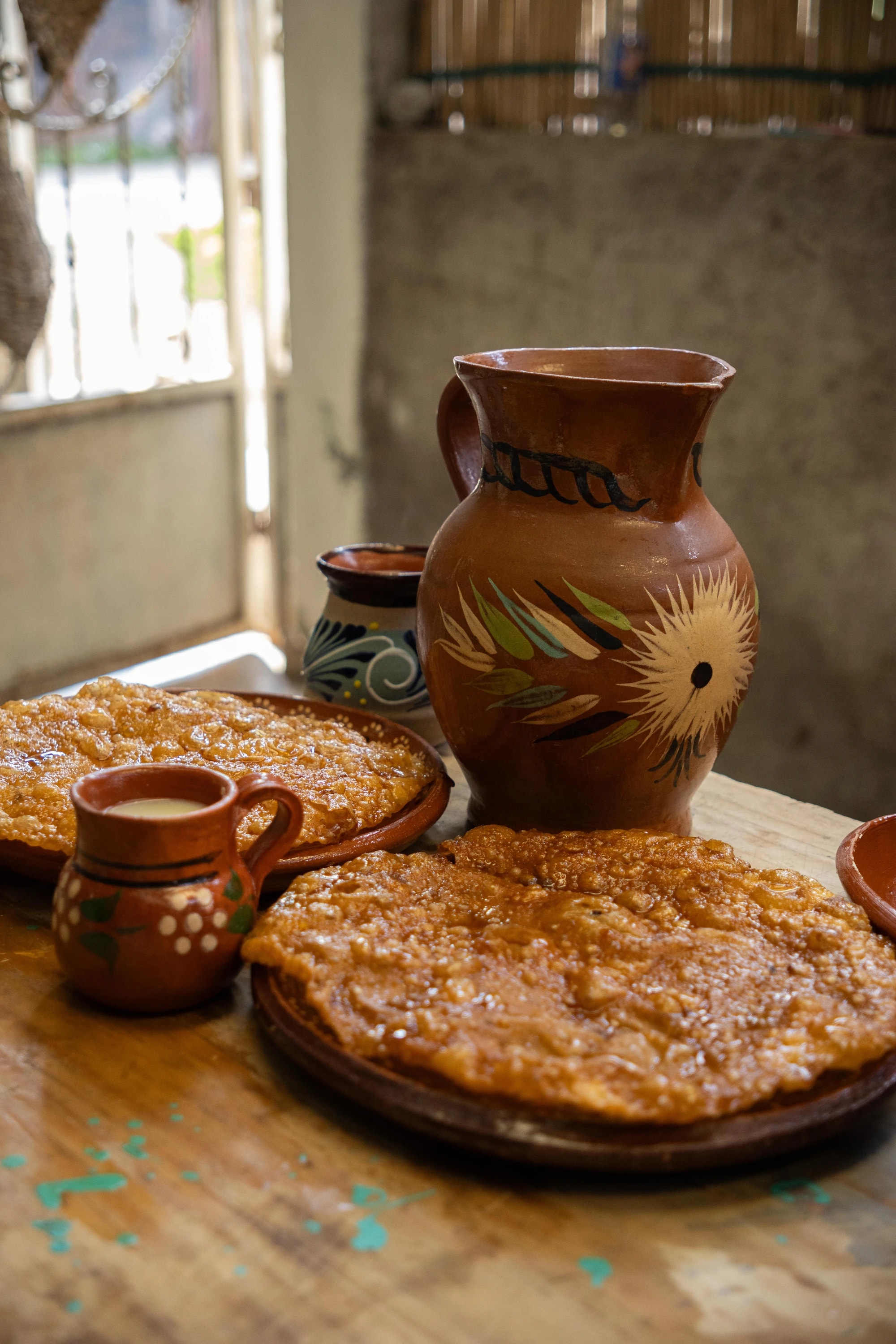 Buñuelos dorados y atole servidos en platos, tazas y jarras de barro sobre una mesa