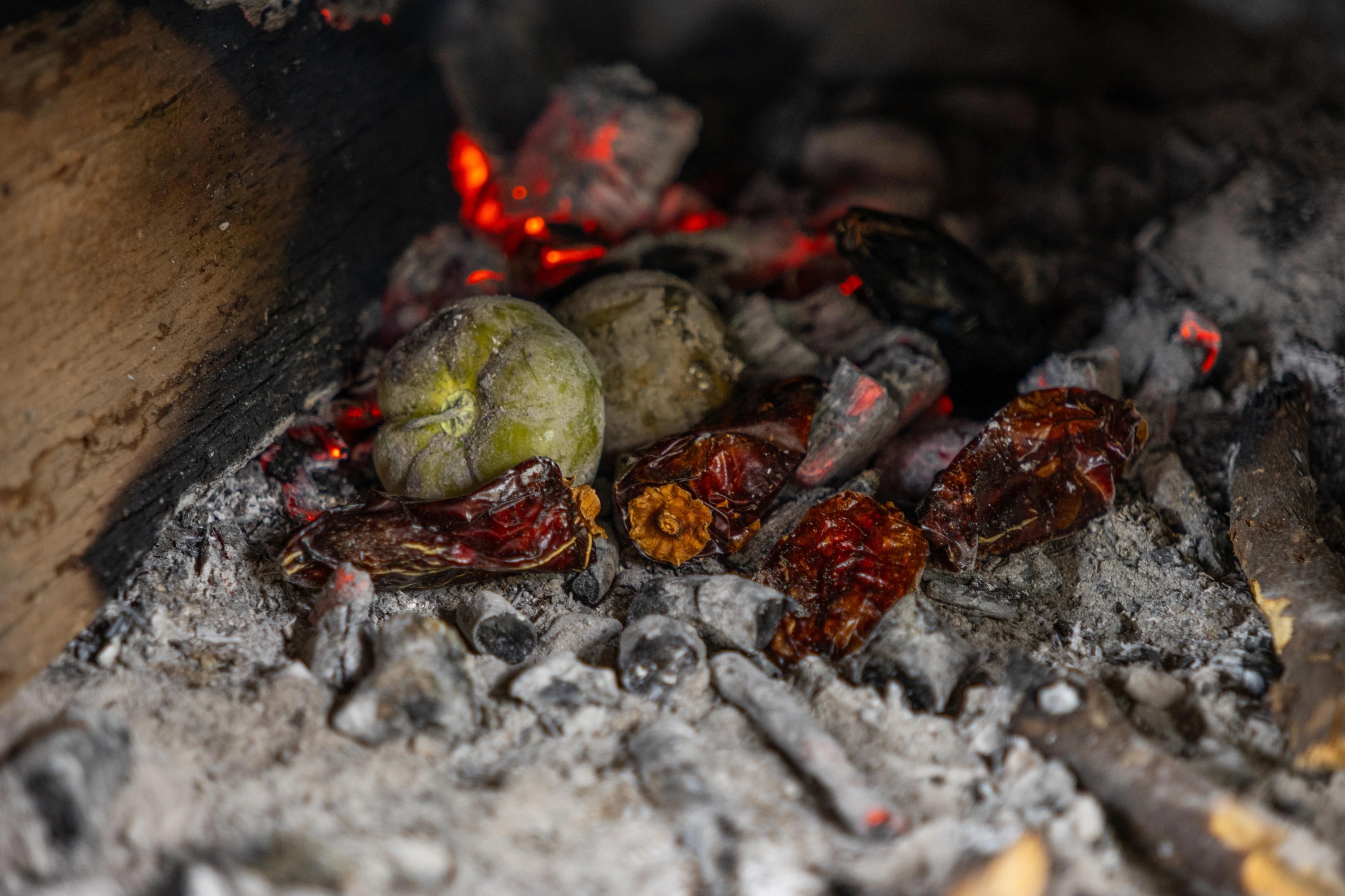 Chiles y jitomates asándose sobre brasas de leña dentro de un horno